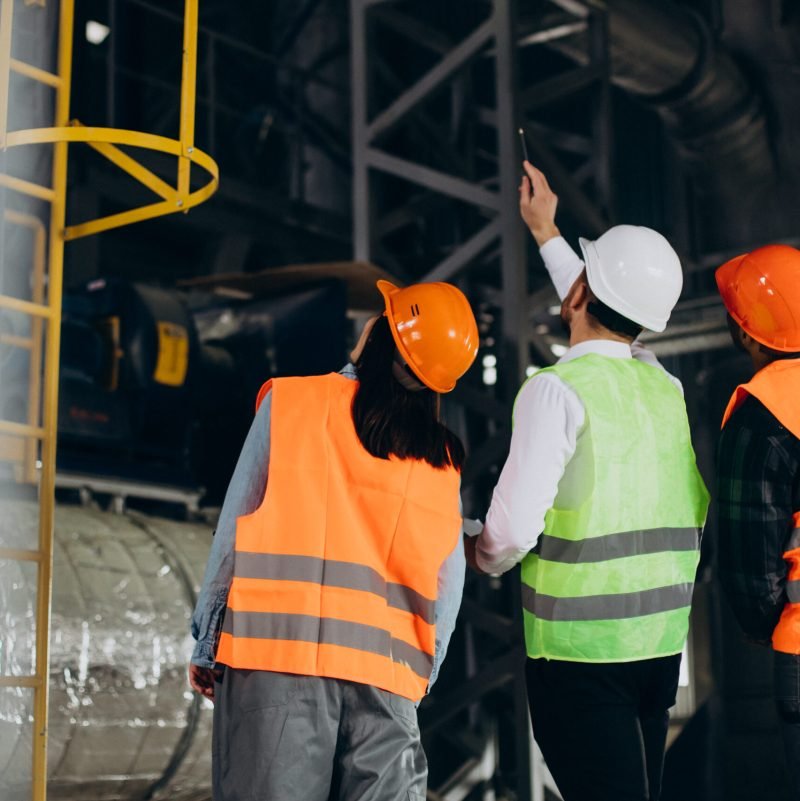 Three factory workers in safety hats discussing manufacture plan